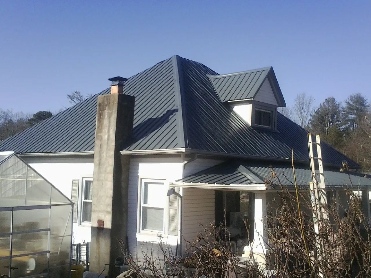 Dark blue standing seam metal roof on a white farmhouse with dormer — Slate & Tile Roof Repair by Roofing Brothers in Marcy