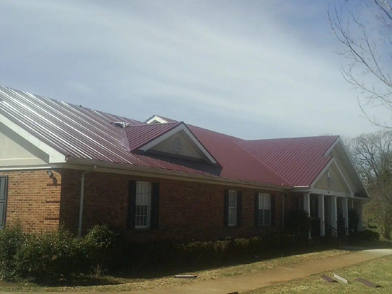 Red metal roof with gabled entries on a long brick building, from a Hail Damage Roof Repair job in Marcy