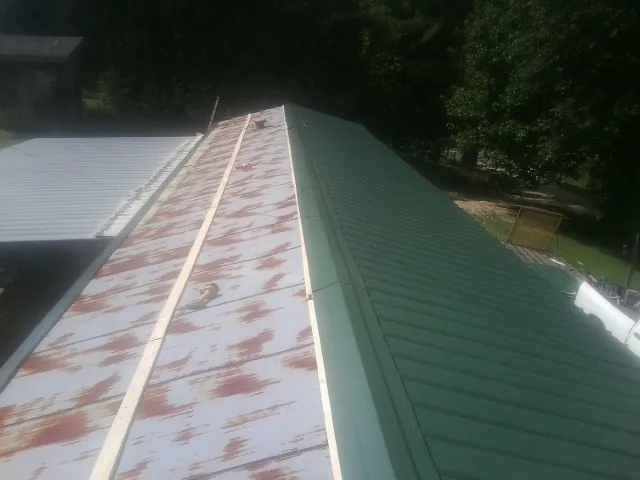 Old rusted panels beside newly installed green metal roofing — Wind Damage Roof Repair by Roofing Brothers in Marcy