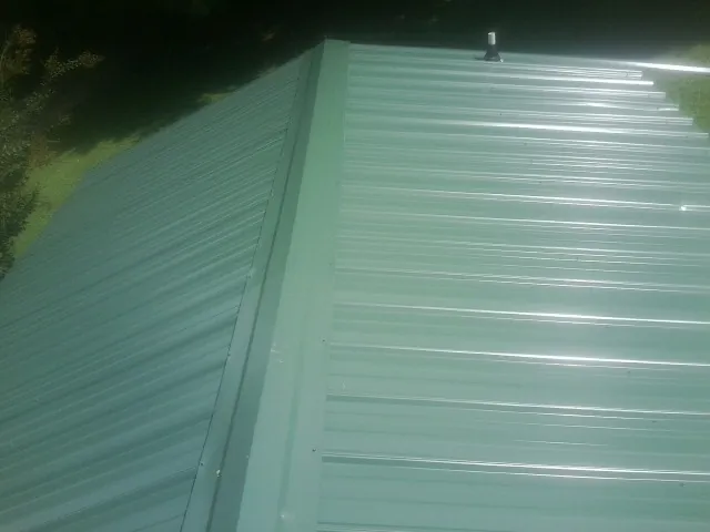 New green metal panels meeting at the ridge of a roof — Flat Roof Repair work by our crew in Marcy