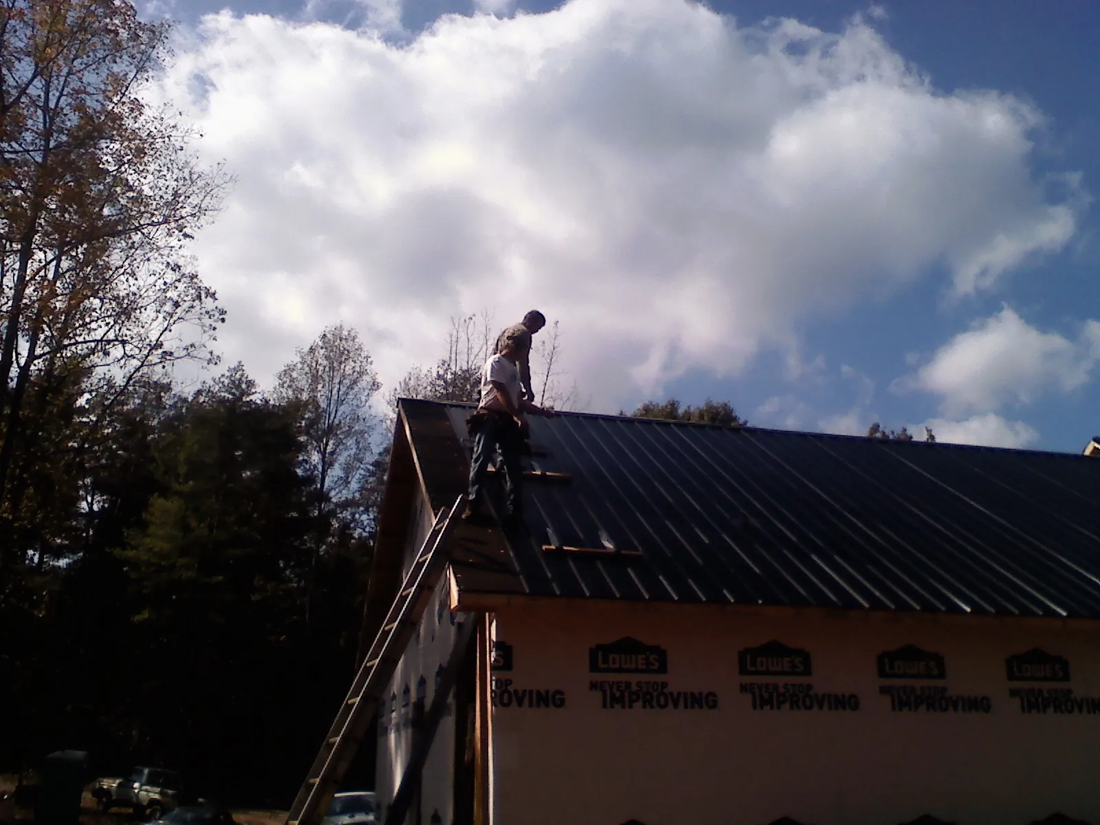 Roofer fastening dark metal panels high against a cloudy sky, from a Roof Inspection job in Marcy