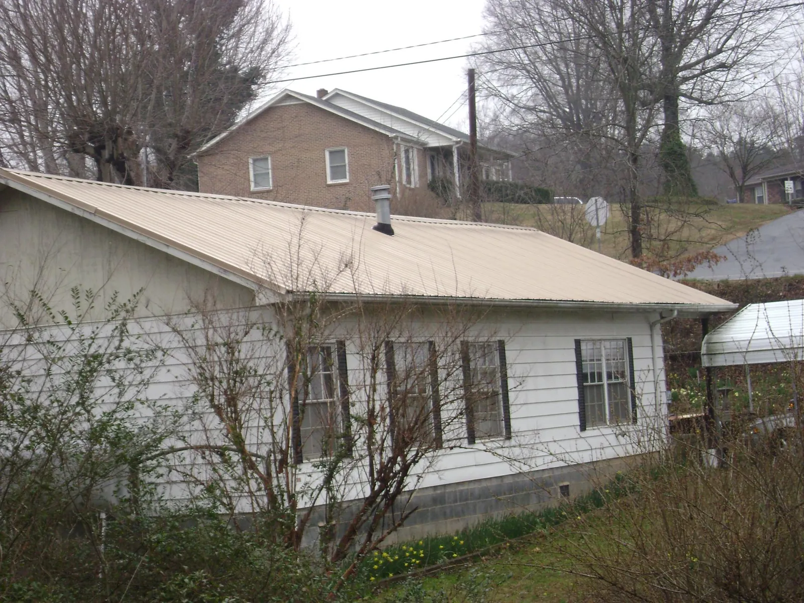 Tan metal roof on a white sided house set into a hillside — Commercial Roofing by Roofing Brothers in Marcy